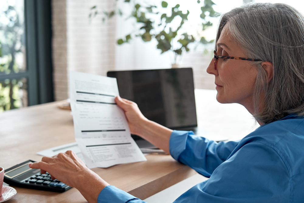 Senior,mature,business,woman,holding,paper,bill,using,calculator,,old