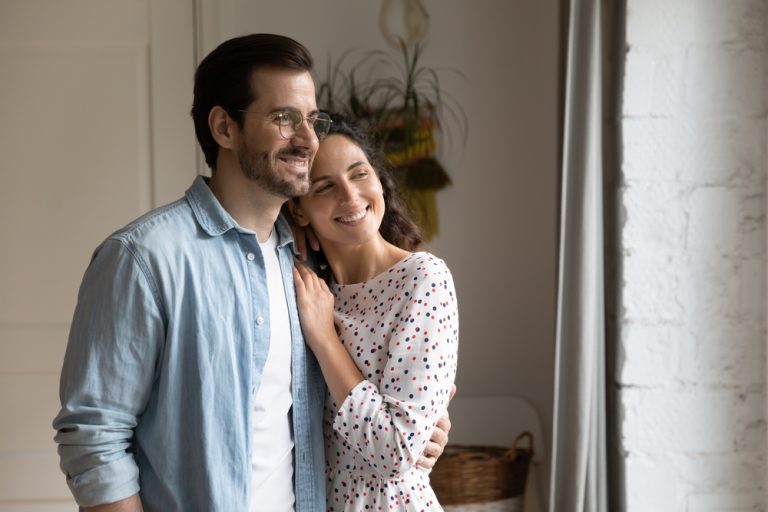 Lovely,married,couple,embracing,standing,indoor,look,into,distance,lost